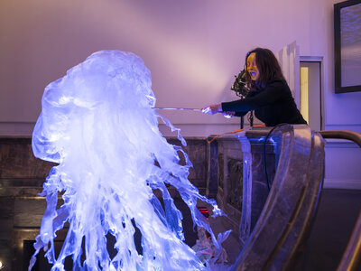 Eine Frau mit Maske steht im Treppenaufgang zum Leibniz-Saal, sie hält eine sich-bewegende Qualle aus filigranem Plastik, die über dem Saal zu schweben scheint