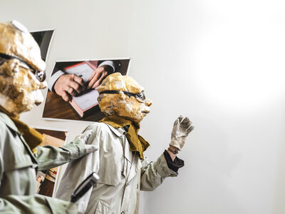 Zwei maskierte Personen in Trenchcoats laufen vorbei an Bildern der Ausstellung "Boris Pistorius. Aufbruch"